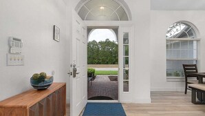 A hallway with a wooden console, a door leading to an outdoor area, and a dining table with chairs.