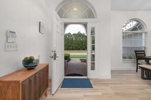 A hallway with a wooden console, a door leading to an outdoor area, and a dining table with chairs.