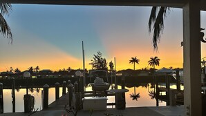 A marina at sunset with boats docked, a dock extending into calm water, and a row of houses in the background. - Beautiful waterfront 3/2 home with dock and boat lift. Cabana Club included! (Key Colony Beach)