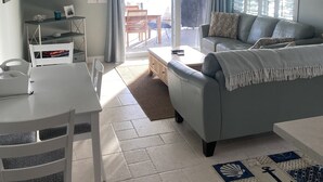 A modern living room with a grey sofa, a white coffee table, a dining table with chairs, a flat-screen TV mounted on the wall, and a ceiling fan. - Beautiful waterfront 3/2 home with dock and boat lift. Cabana Club included! (Key Colony Beach)