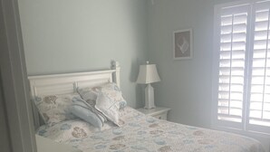 A bedroom with a bed, a nightstand, a ceiling fan, a window with blinds, and a wall-mounted artwork. - Beautiful waterfront 3/2 home with dock and boat lift. Cabana Club included! (Key Colony Beach)