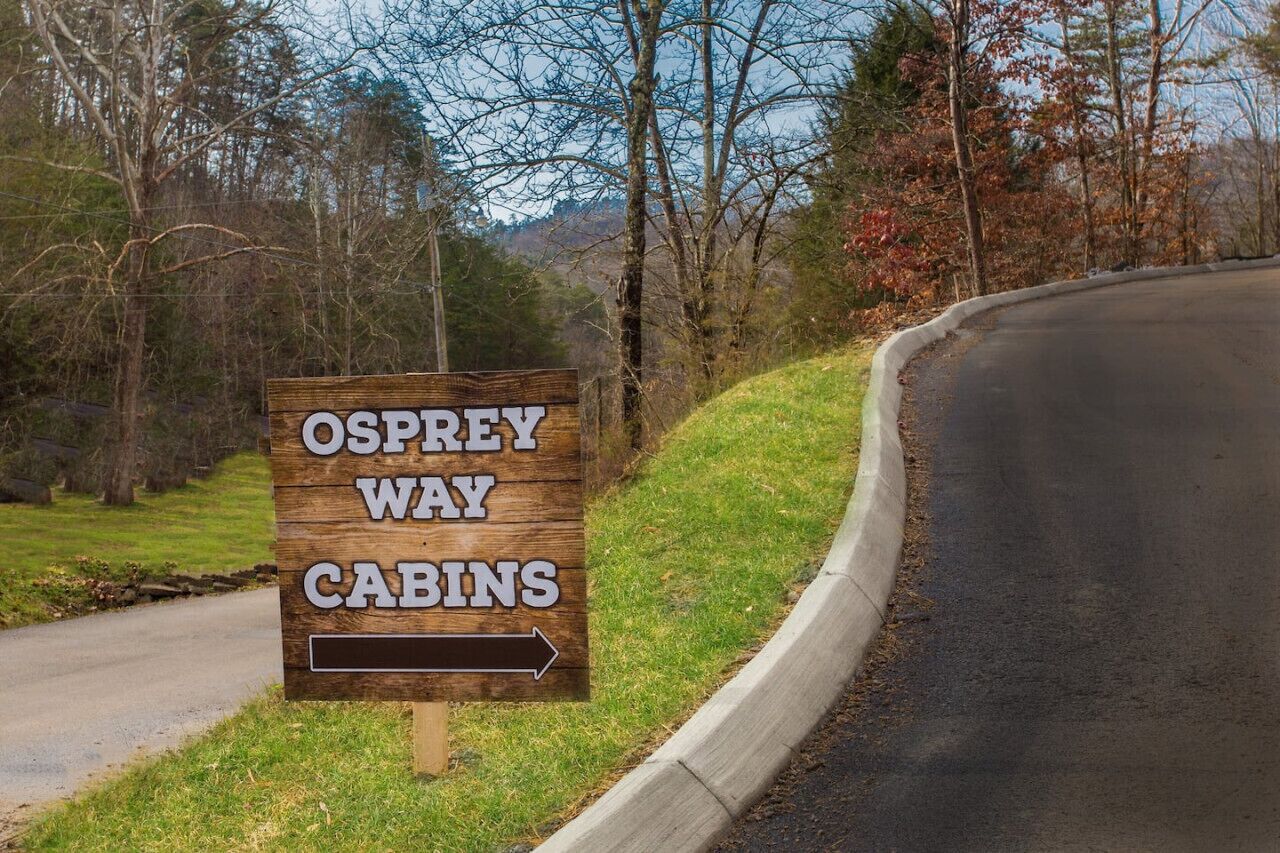 Un panneau en bois indiquant « Osprey Way Cabins » avec une flèche pointant vers la droite.