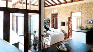 A spacious living area with a high ceiling, a stone wall, a white sofa, a dining table, and a kitchen area with a counter and cabinets.