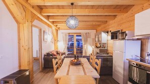 Interior de madera con una mesa de comedor, sillas, una zona de cocina con electrodomésticos y una vista por un vano.