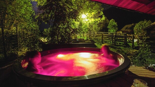 Un jacuzzi en un jardín nocturno, con árboles y una terraza de madera.