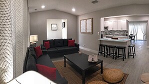 A modern living room with a dark sofa, a coffee table, and a kitchen area with bar stools. - 3-Bedroom Heated Private Pool Vacation Home just minutes from the Beach Pet (Deerfield Beach)