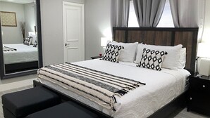 A modern bedroom with a large bed, two bedside tables, a mirror, and a view of a room with a bed and a picture frame. - 3-Bedroom Heated Private Pool Vacation Home just minutes from the Beach Pet (Deerfield Beach)