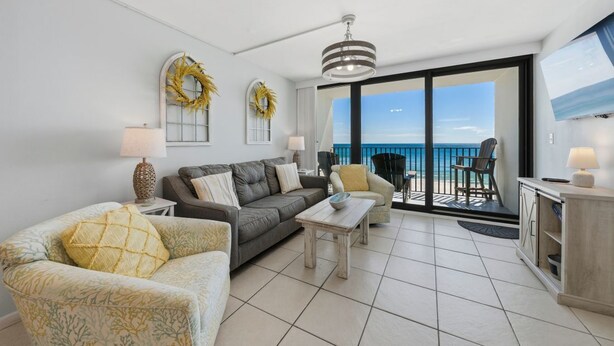 A living room with a sofa, armchair, coffee table, and a view of the ocean through large sliding doors.