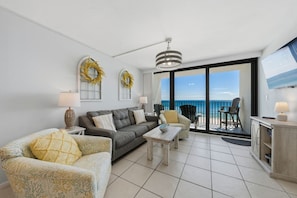 A living room with a sofa, armchair, coffee table, and a view of the ocean through large sliding doors. - Island Sunrise 565- Epic Vacations Start Here! Book Now! (Gulf Shores)