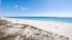 A beach with a clear sky, sandy shore, and a pier in the distance.