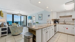 A modern kitchen with white cabinets, a marble countertop, and a view of the ocean.