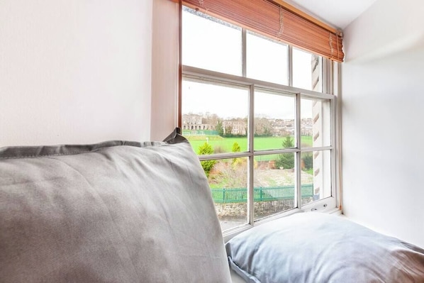 Ein Zimmer mit einem großen Fenster, einem grünen Zaun und einem Gebäude im Hintergrund.