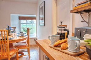 Ein Essbereich mit einem Holztisch, Stühlen, einer Kaffeemaschine und einem Fenster mit Jalousien.