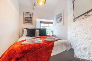 Ein Schlafzimmer mit einem Bett, Kissen, einer roten Decke und zwei gerahmten Bildern an der Wand.