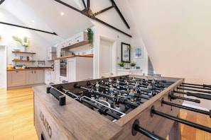 A modern kitchen with a foosball table, wooden cabinets, and a lofted dining area.