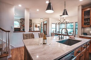 A modern kitchen with a large island, a stone accent wall, and a chandelier.