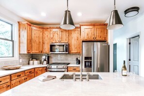 A kitchen with wooden cabinets, stainless steel appliances, a large island with a sink, and pendant lighting.