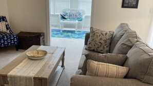A living room with a sofa, a coffee table, and a wicker chair. There is a starfish decoration on the wall and a framed picture. - Beautiful beach bliss (Ocean View)