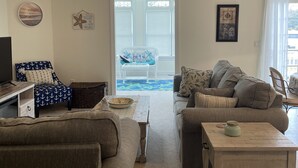 A living room with a ceiling fan, a television, a sofa, a coffee table, and a view of the outdoors through a window. - Beautiful beach bliss (Ocean View)