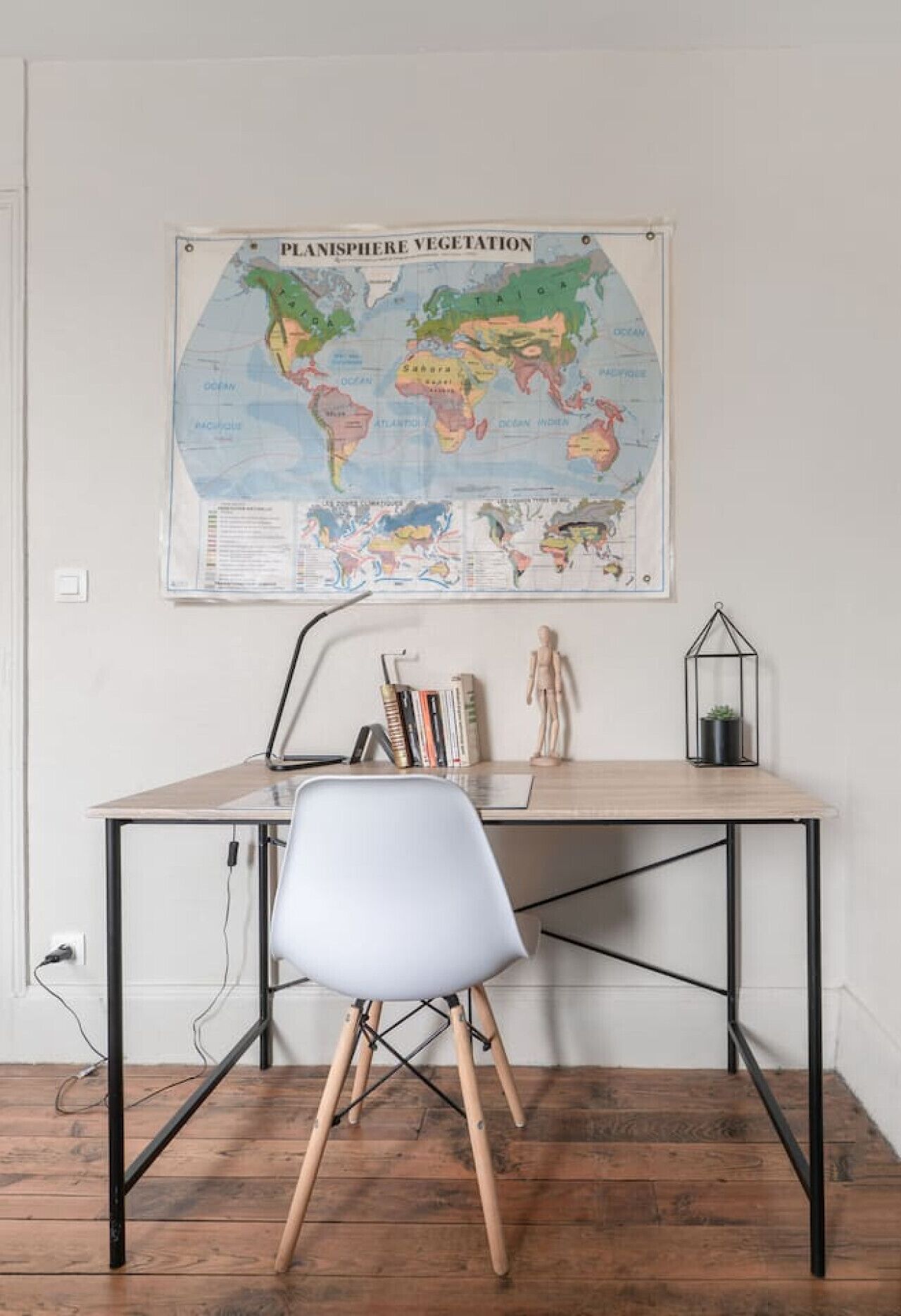Een bureau met een wereldkaart, een witte stoel, een kleine beeldje en een plant in een glazen vaas.