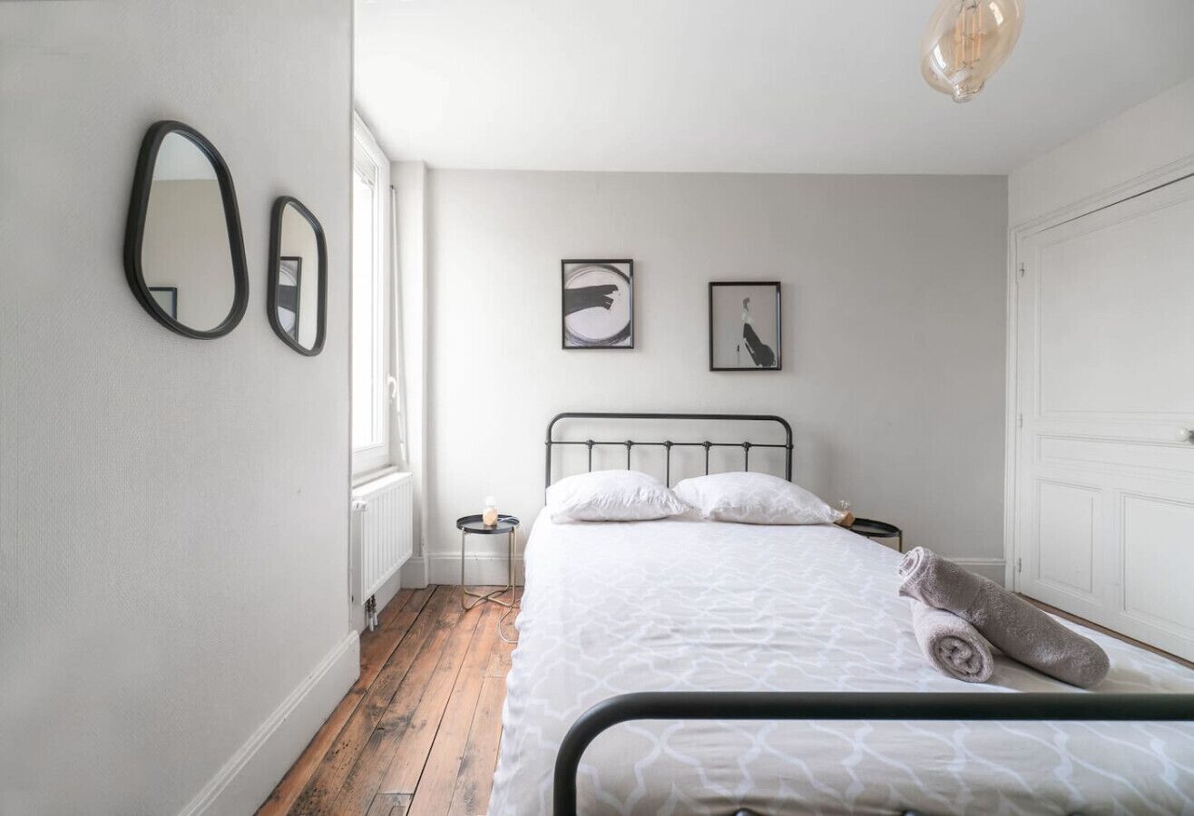 A bedroom with a bed, a radiator, a window, and two framed pictures on the wall.