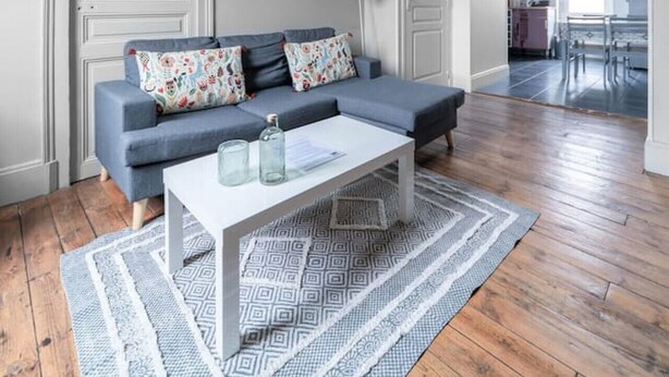 Una sala de estar moderna con un sofá gris, cojines estampados, una mesa de centro blanca y una alfombra con diseño.