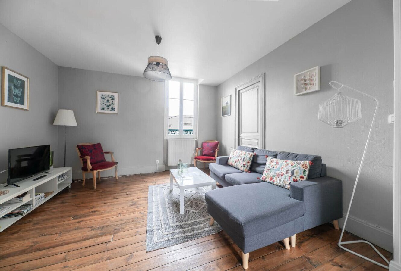A modern living room with a grey sofa, a coffee table, a TV on a white stand, and a red chair.