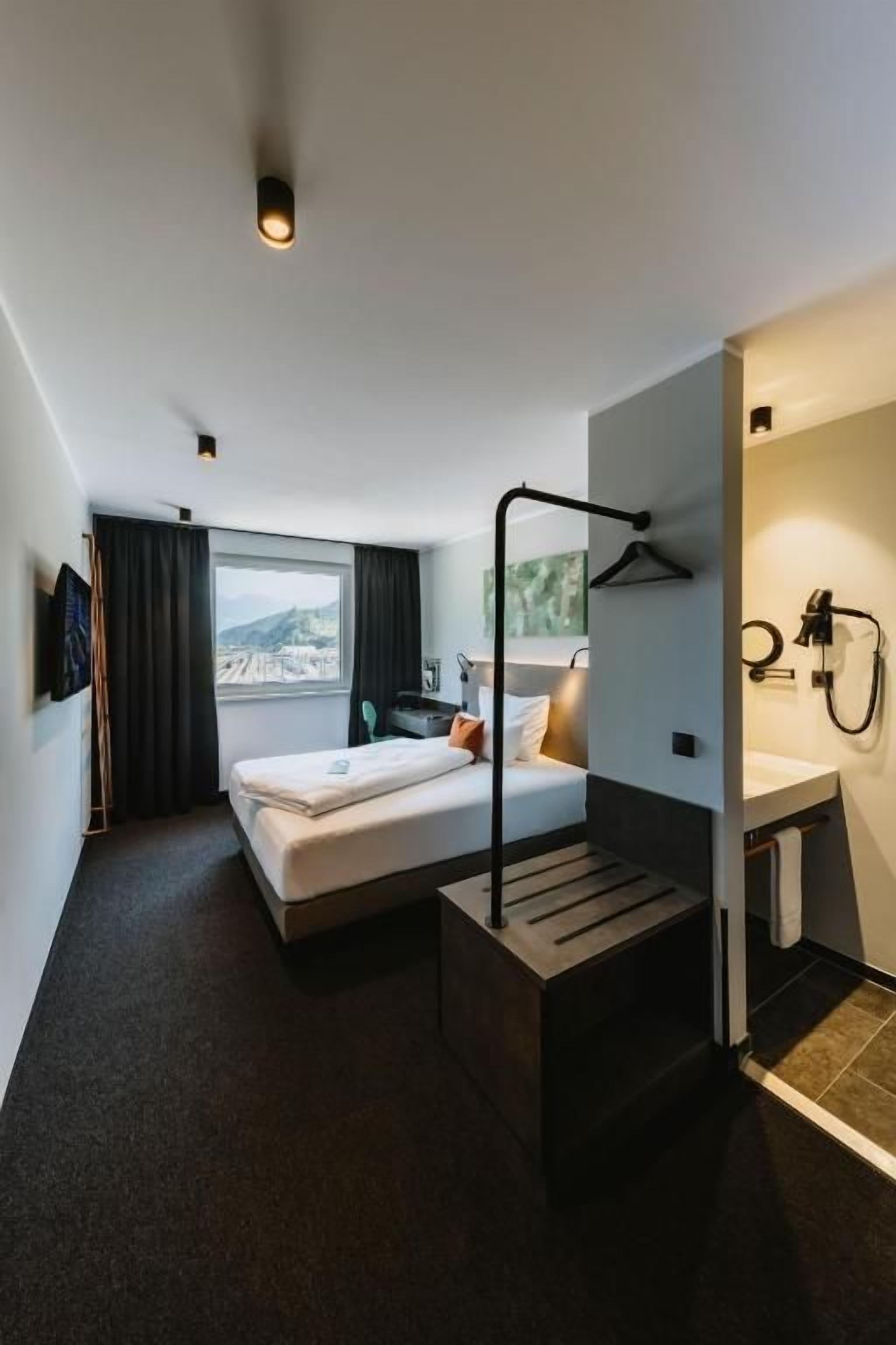 Ein modernes Hotelzimmer mit Bett, Nachttisch und Blick auf die Stadt.