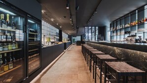 A bar area with a long counter, stools, and shelves with bottles and glasses.