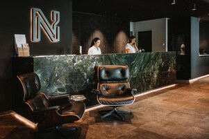 Un área de recepción con mostrador de mármol, sillas de cuero y un gran letrero iluminado con la letra 'N'.