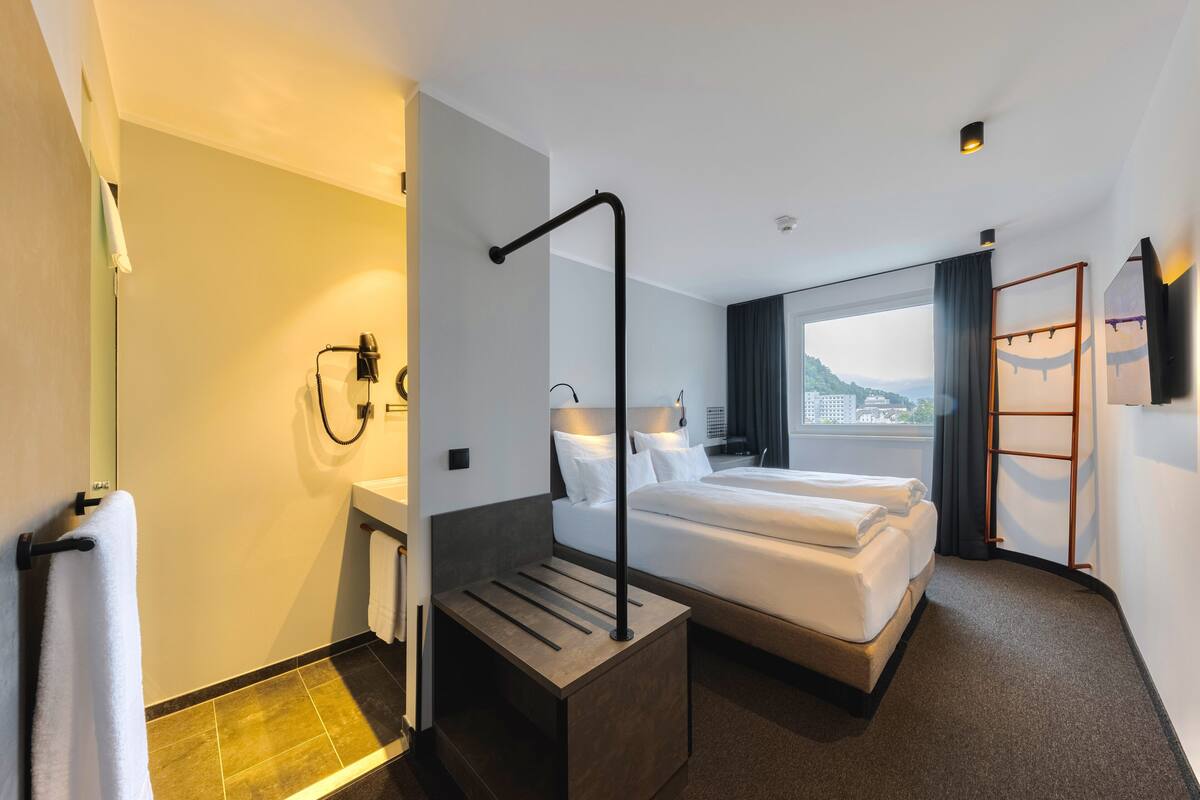 Ein Hotelzimmer mit Bett, Schreibtisch, Stuhl, Duschbereich und einem Fenster mit Aussicht.