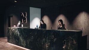A reception desk with a marble top, a large illuminated 'N' sign, and two receptionists.