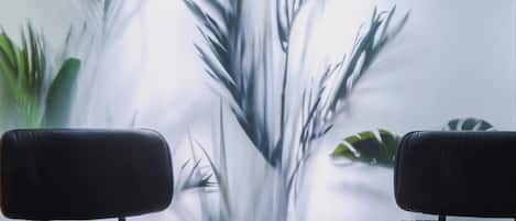 Una habitación con dos sillones de cuero negro frente a una pared con un mural borroso de plantas.