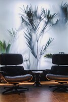 Una habitación con dos sillones de cuero negro frente a una pared con un mural borroso de plantas.