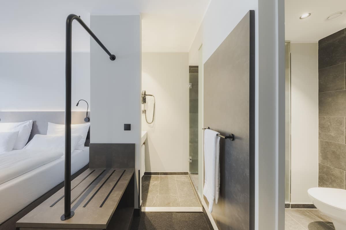 Ein modernes Hotelzimmer mit Bett, Nachttisch, Duschbereich und Toilette.