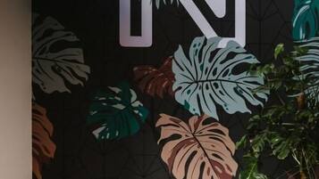 Zona de recepción con un gran mural en la pared, dos sillas negras, una mesita y una planta en maceta.