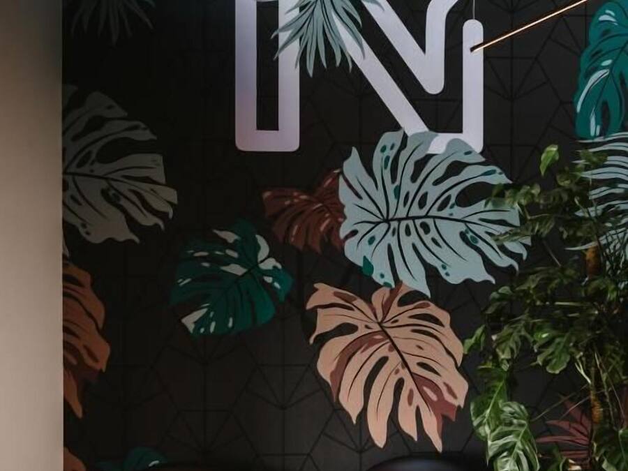 Zona de recepción con un gran mural en la pared, dos sillas negras, una mesita y una planta en maceta.