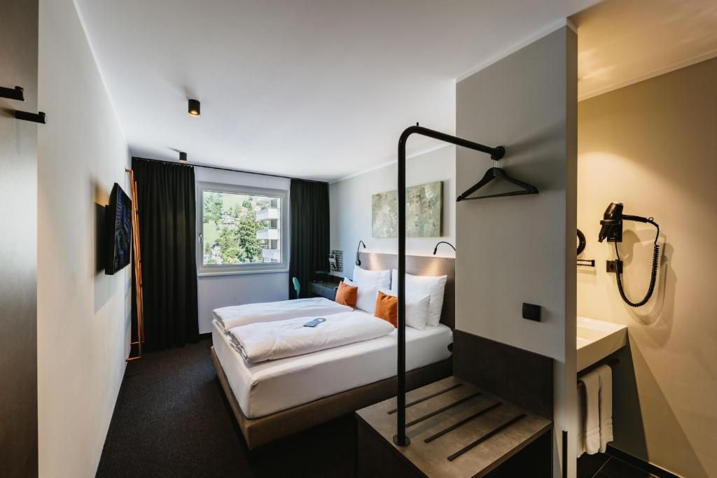 Una camera d'albergo con un letto, una scrivania, una sedia, una finestra e un bagno.