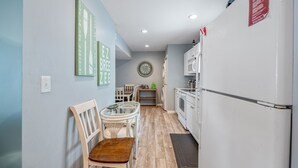 A kitchen with white cabinets, a refrigerator, a microwave, a dining table with chairs, and a wall clock.