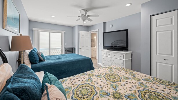 A bedroom with a bed, a TV, a ceiling fan, and a window.