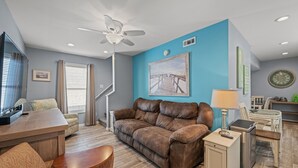 A modern living room with a brown leather sofa, a wooden coffee table, a small cabinet, and a ceiling fan.