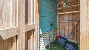 A wooden shed with a green exterior, a metal water spigot, a hose, a broom, and a trash bin.