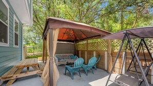 A covered patio area with a swing set, a wooden table, and two chairs.
