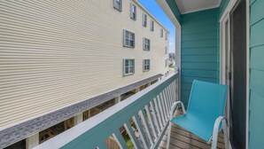 Een balkon met een blauwe stoel, een witte balustrade en een gebouw met beige gevelbekleding en meerdere ramen.