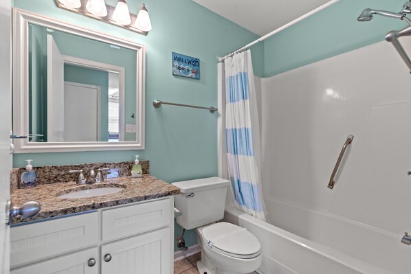 A bathroom with a white toilet, a granite countertop sink, a mirror, and a shower with a white curtain. - Hyperion 401 Oceanfront 3BR 2BA with Outdoor Pool (North Myrtle Beach)