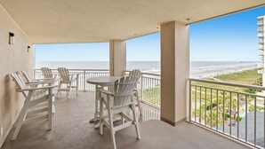 Een balkon met uitzicht op het strand, met een tafel en stoelen.