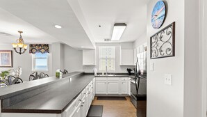 Een moderne keuken met witte kastjes, een granieten aanrechtblad, een roestvrijstalen koelkast en een decoratieve klok.
