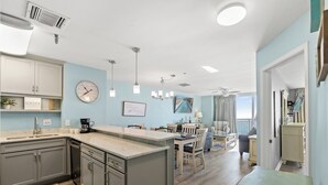 A modern kitchen with a central island, a dining area with a chandelier, and a view of the outdoors. - Hyperion 604 Oceanfront Sleeps 8-Outdoor Pool (North Myrtle Beach)