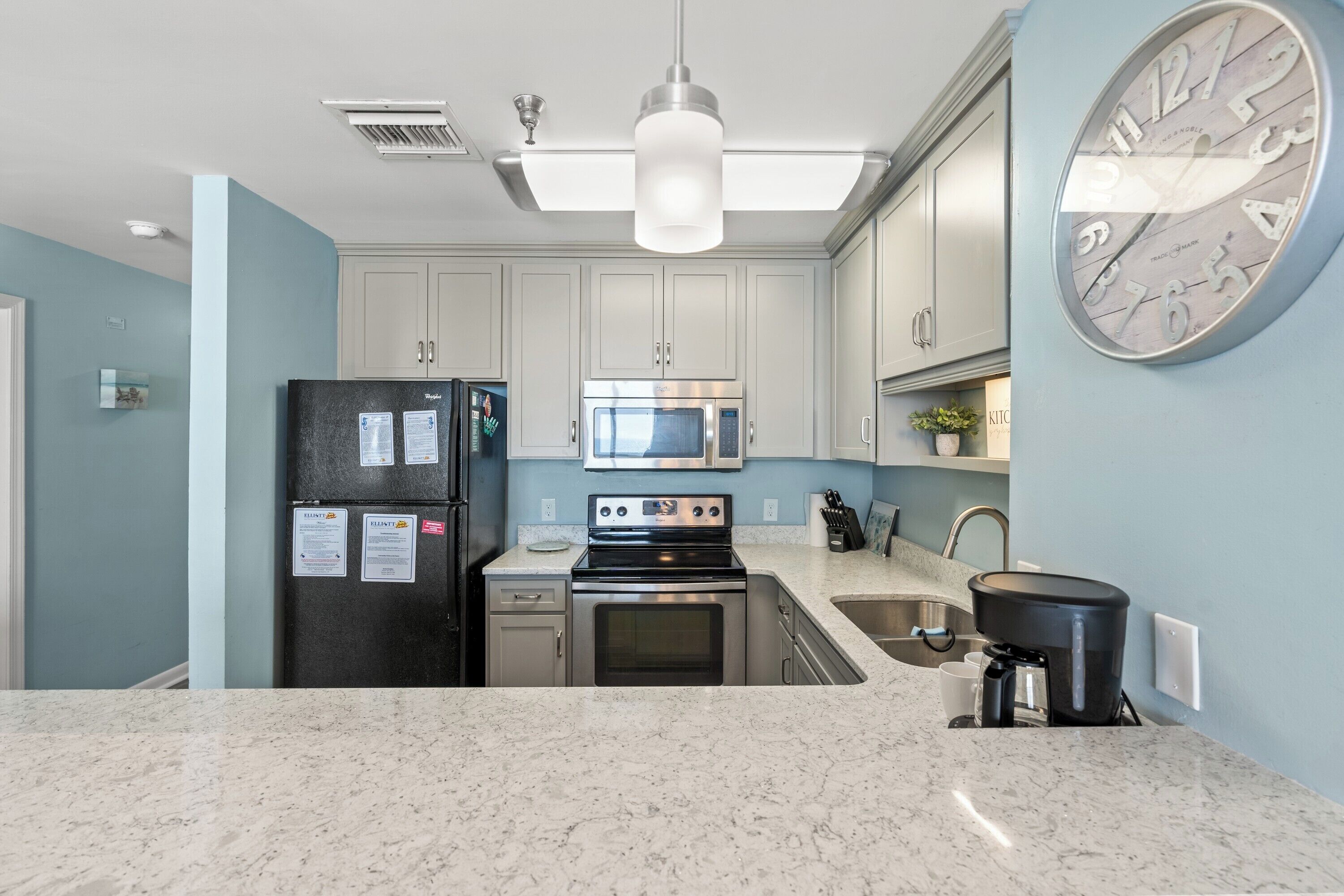 A modern kitchen with white cabinets, a stainless steel refrigerator, a microwave, an oven, a sink, and a coffee maker.