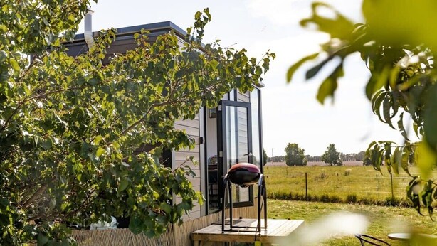 A modern house with a glass enclosure, a wooden deck, and a barbecue grill. - Tiny Balloon House by Tiny Away (Canowindra)